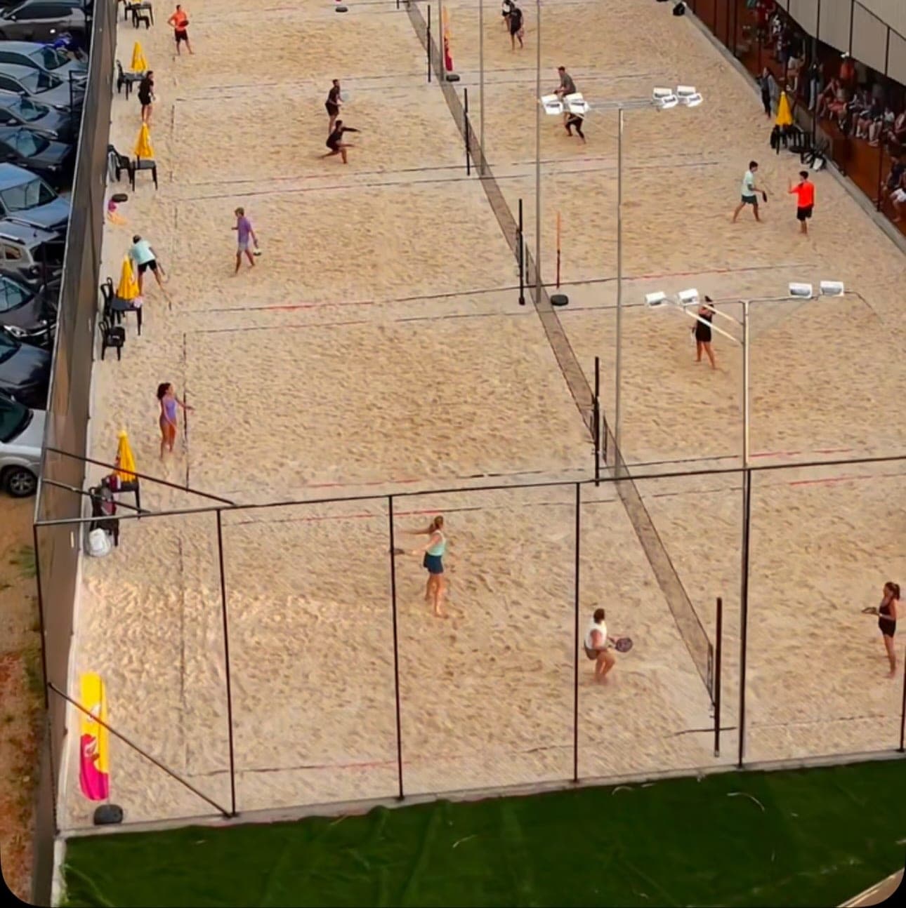 Quadras de areia vistas do alto, cheias de gente jogando beach tennis