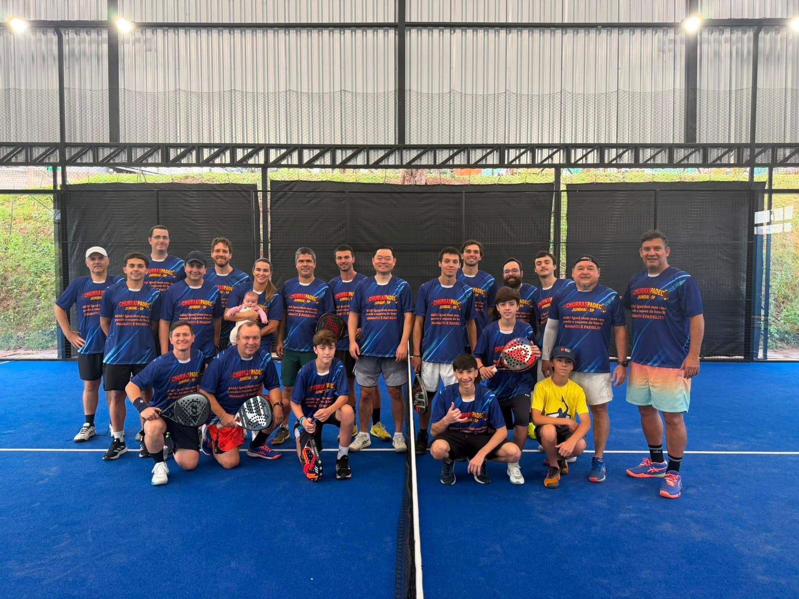 Grupo grande de jogadores com camisetas iguais posando na quadra de padel coberta