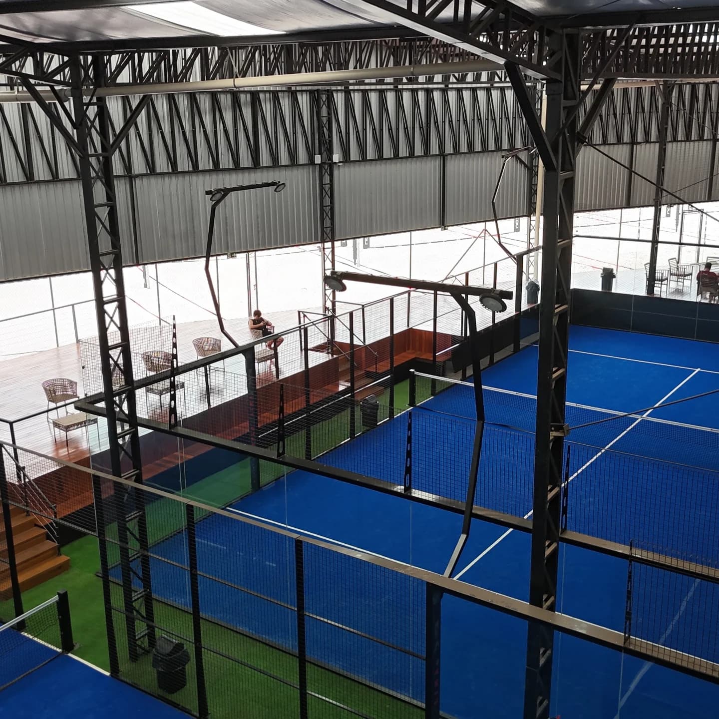 Quadra de padel coberta, piso azul e paredes de vidro, vista do mezanino