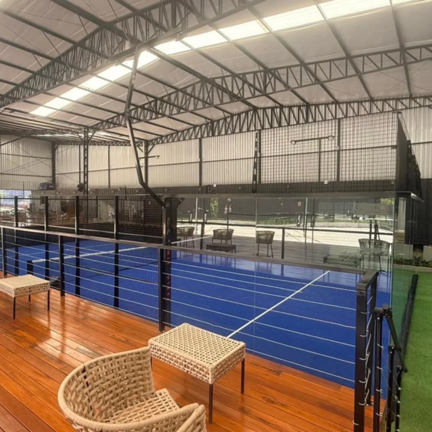 Poltronas de vime no deck de madeira, de frente para a quadra de padel coberta