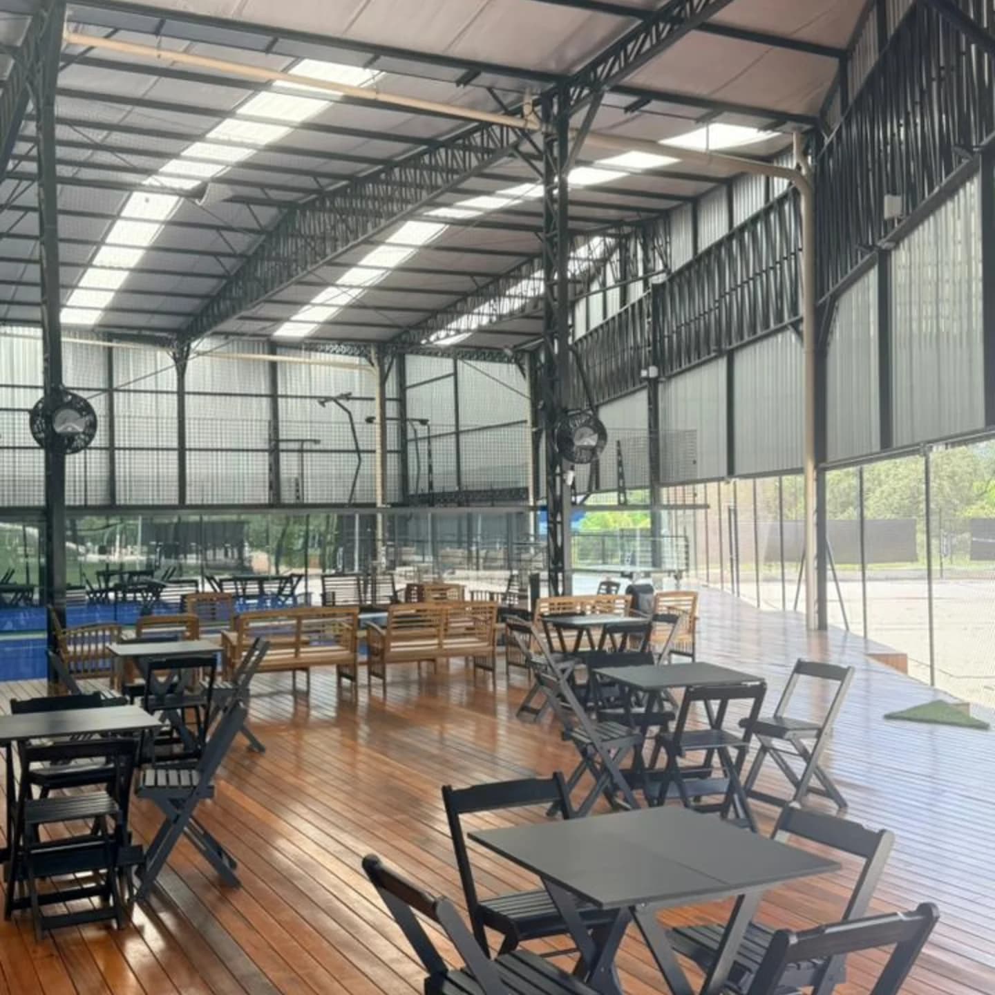 Mesas e cadeiras no deck de madeira coberto, ao lado das quadras